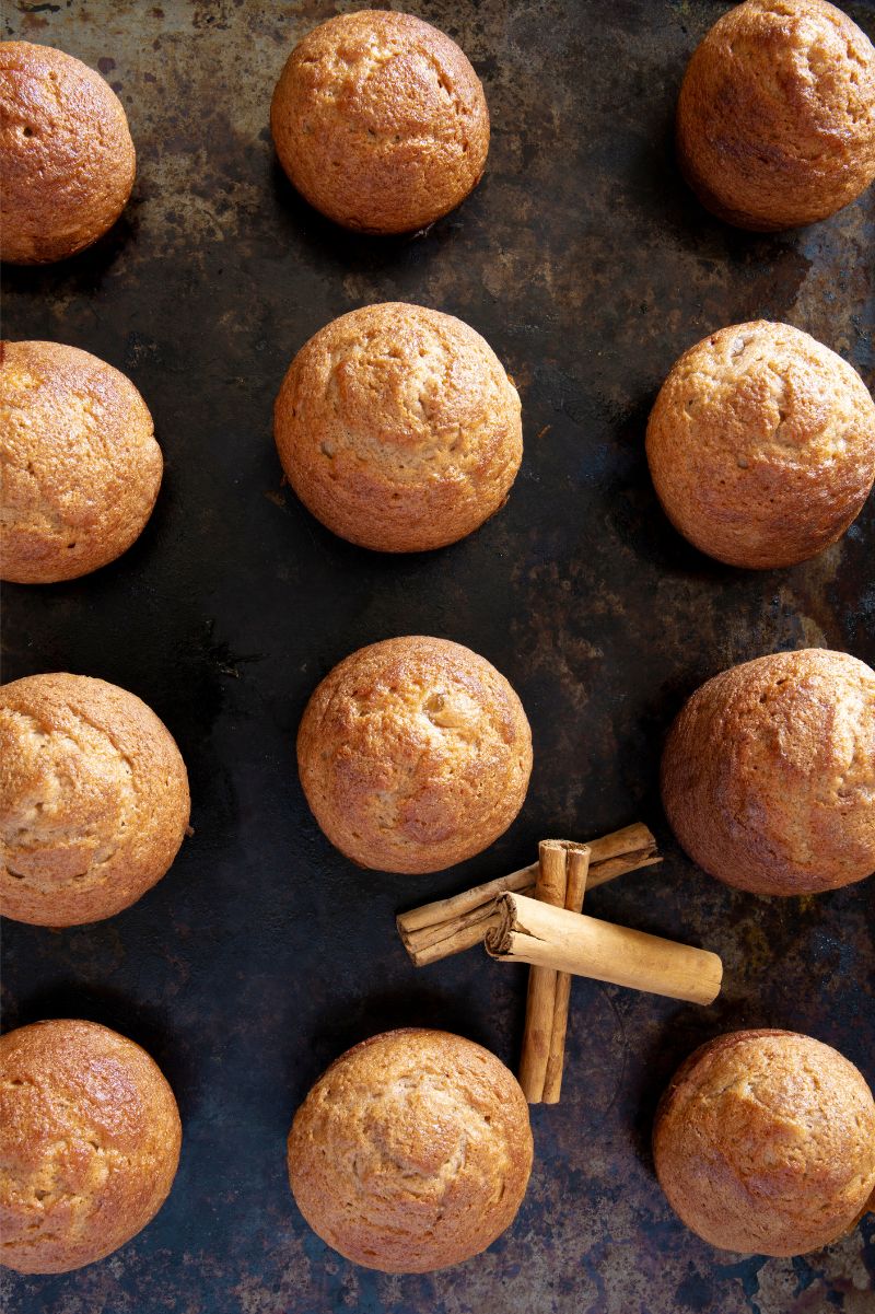 Top view of a dozen apple muffins cooled on a dark background with fragrant cassia bark nestled among them.