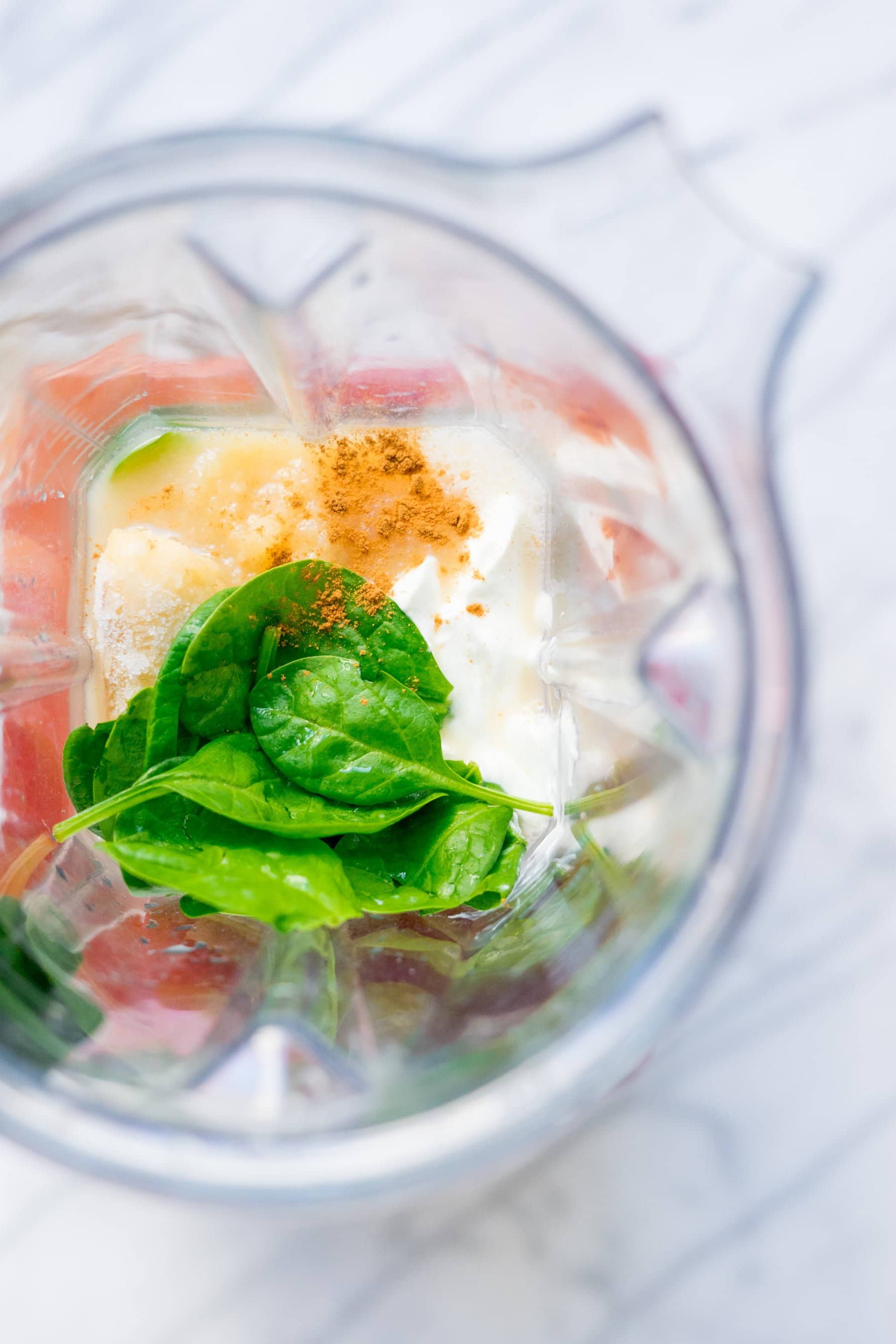 Overhead view of blender with spinach, yogurt, and cinnamon inside carafe