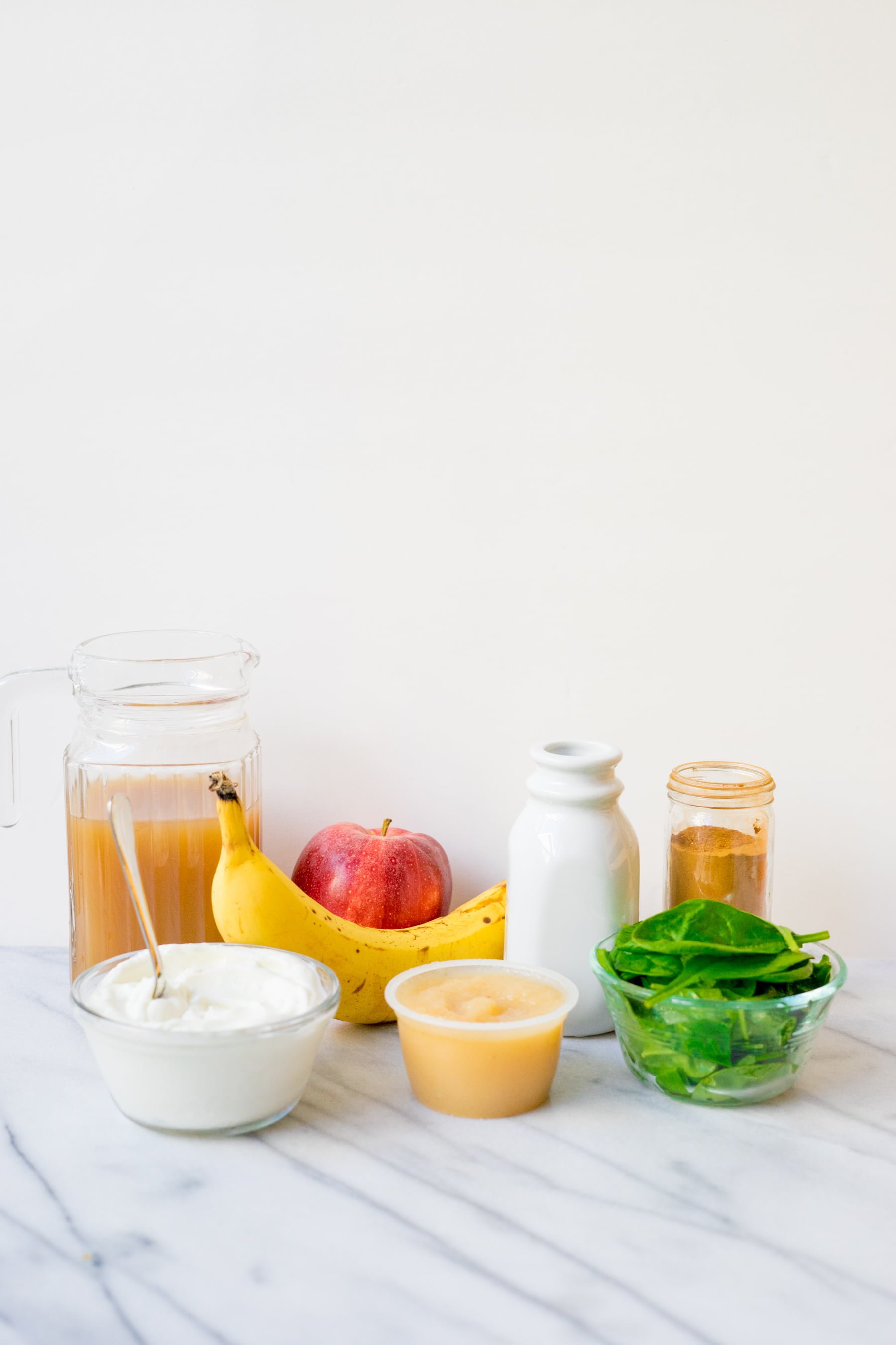 Apple cider, banana, milk, yogurt, spinach, applesauce, cinnamon arranged on kitchen counter