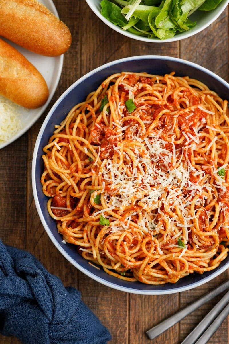 Top view of a pasta arrabbiata dinner served with bread, shredded parmesan cheese, and a side salad.