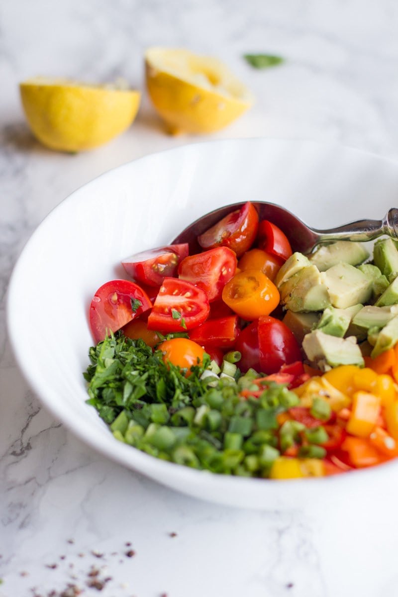 A spoon sits in a bowl of avocado bell pepper salad ingredients