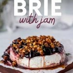 Baked brie with jam garnished with fresh thyme and served on a wooden board. A text overlay reads, "Baked Brie with Jam."