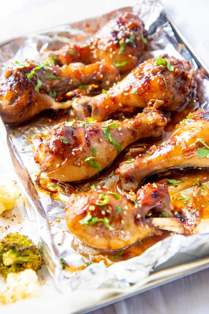 Baked sticky chicken legs garnished with cilantro on half of a foil lined sheet pan.