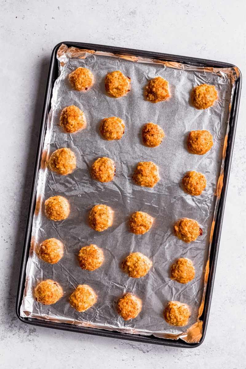 Baked chicken meatballs on a foil lined baking sheet.