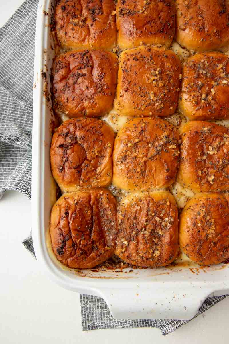 Top view of baked sliders in a white baking dish on a light counter.