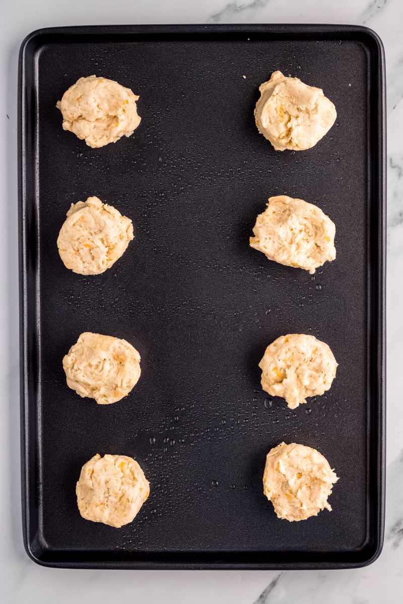 Eight rounds of drop biscuit dough on a greased baking sheet.