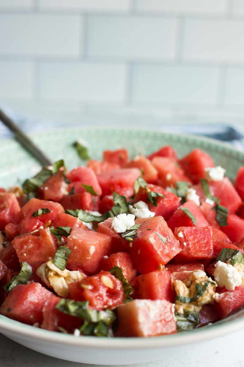 Close view of melon cubes dressed with balsamic vinaigrette and tossed with goat cheese and fresh basil.