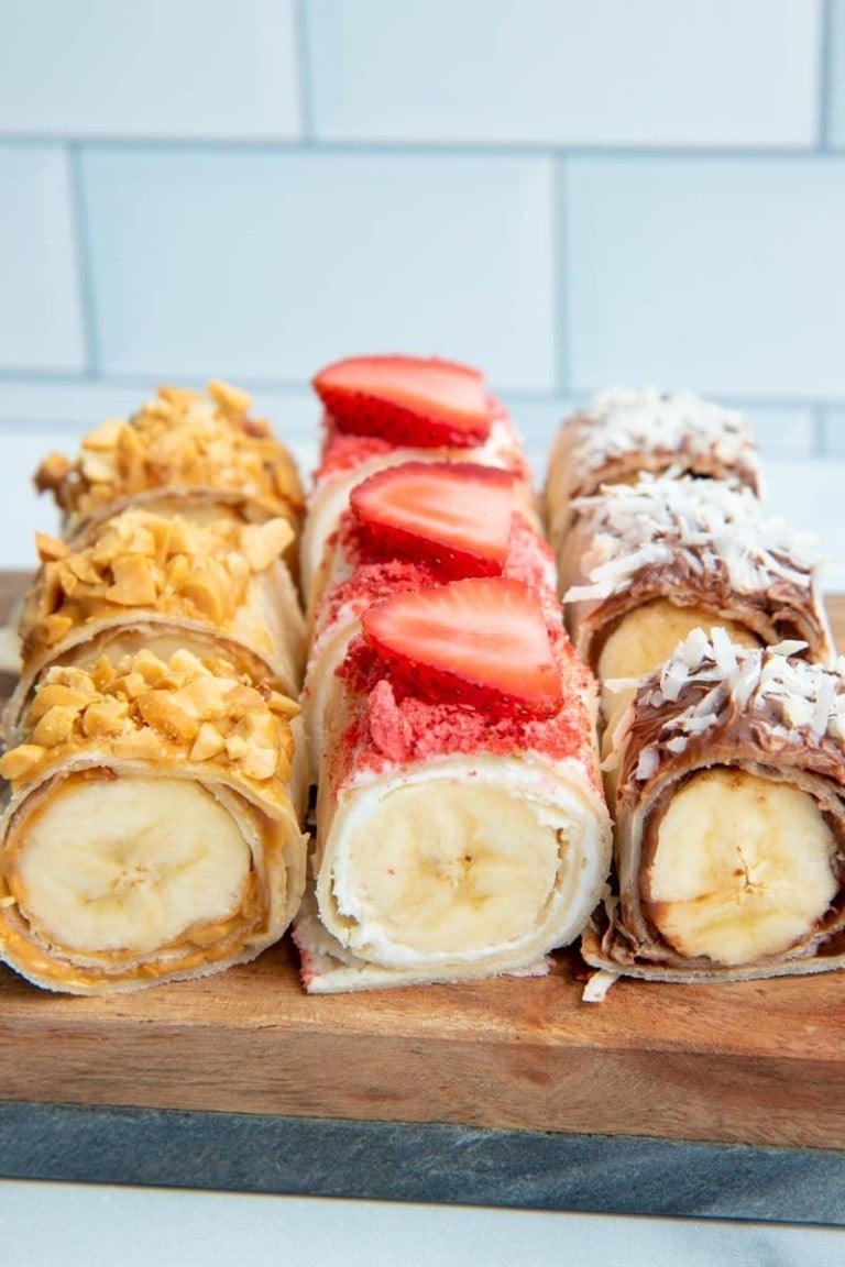 Close view of three flavors of banana sushi served on a wooden platter.