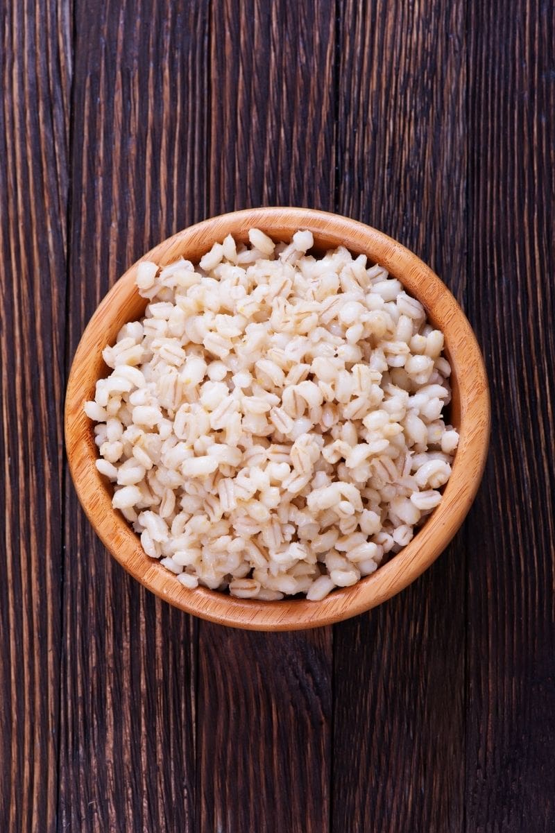 Overhead of cooked barley grains in a wooden bowl.