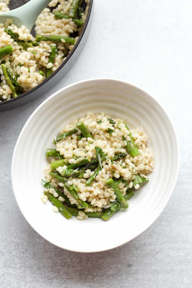 Overhead of barley risotto served in a bowl alongside a skillet of more risotto.