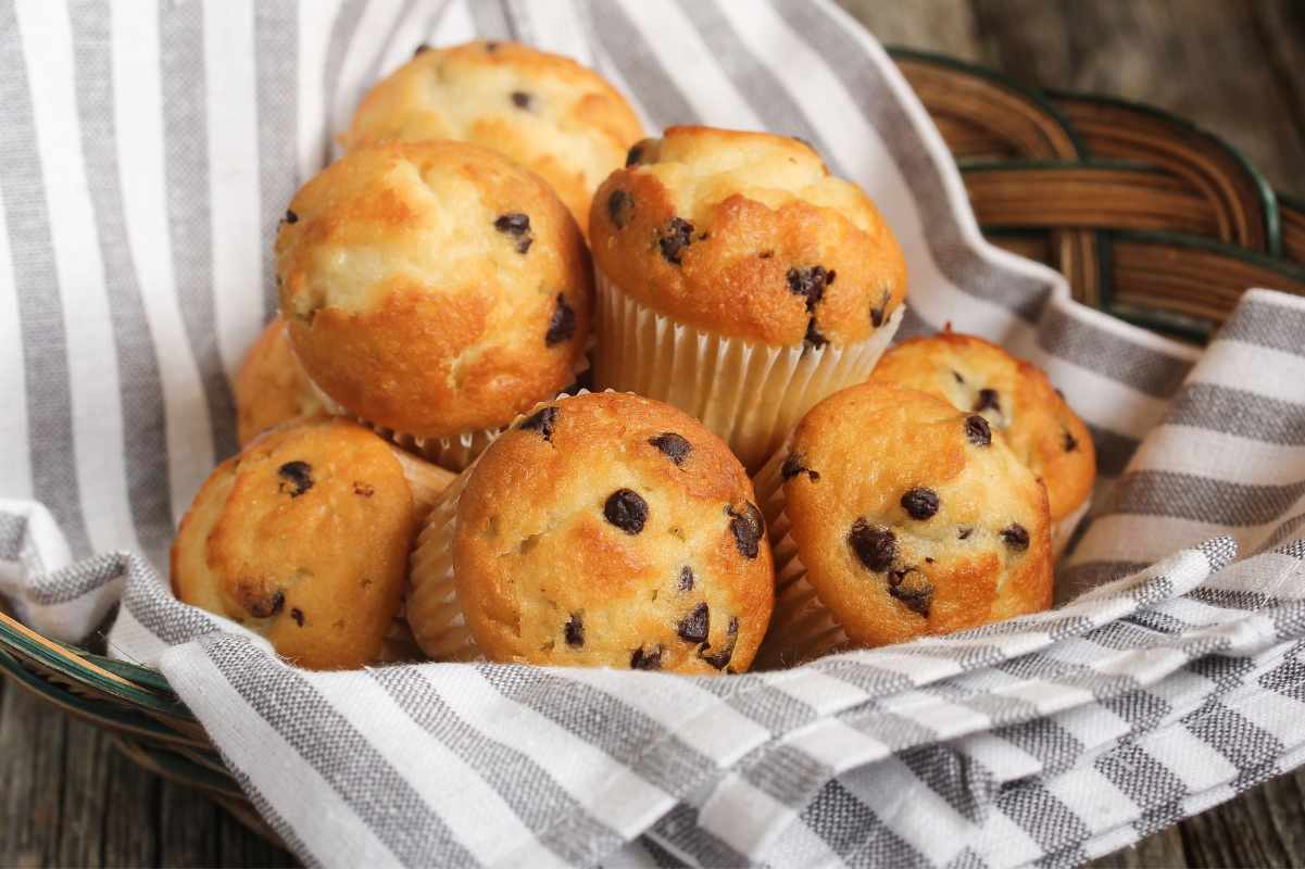 A tea towel lined basket of mini muffins rests on a wooden table.