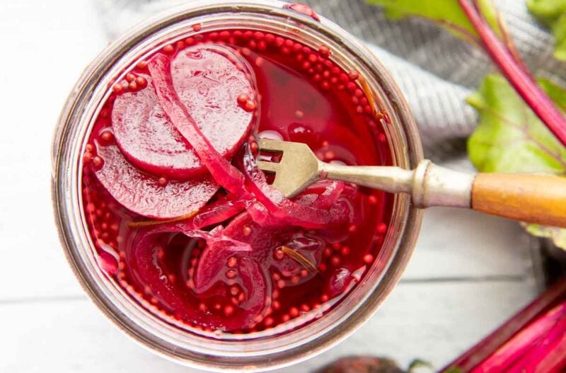 Close view of beet and onion slices in a colorful brine in a mason jar.