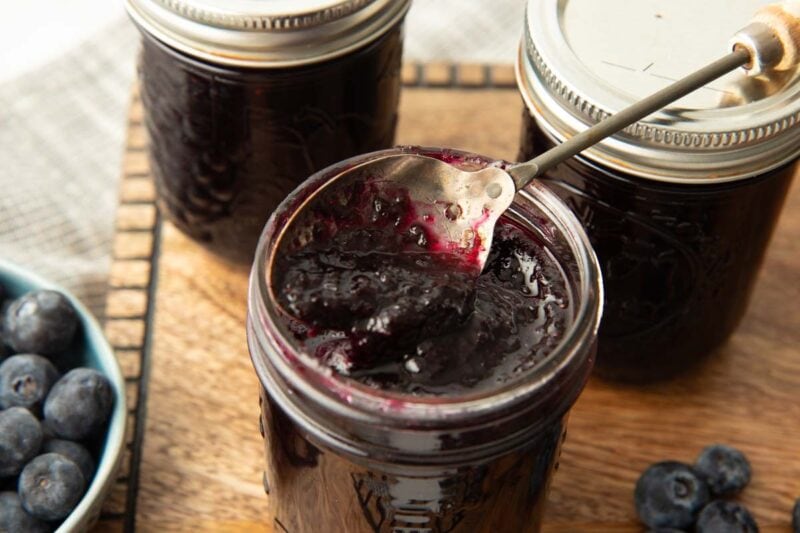 Close view of an open jar of blueberry jam with a spoon dipped into the top.