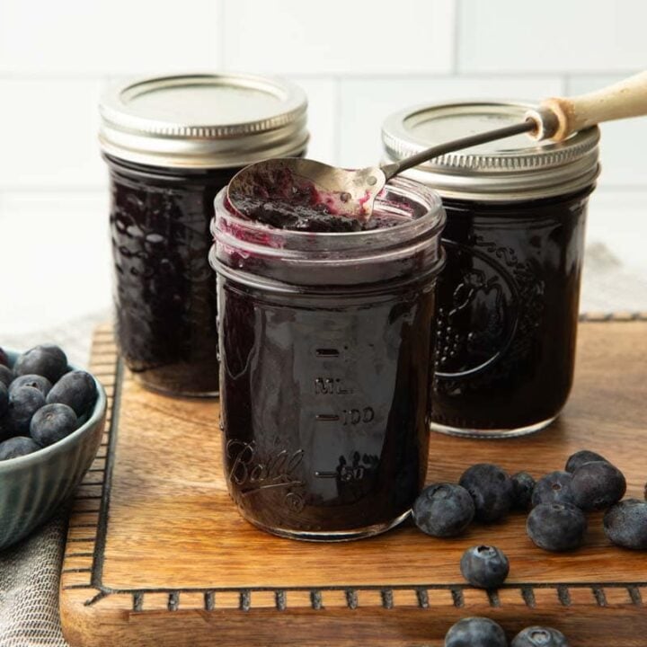 Three half-pint jars of berry jam stand on a wooden cutting board with fresh berries around them.