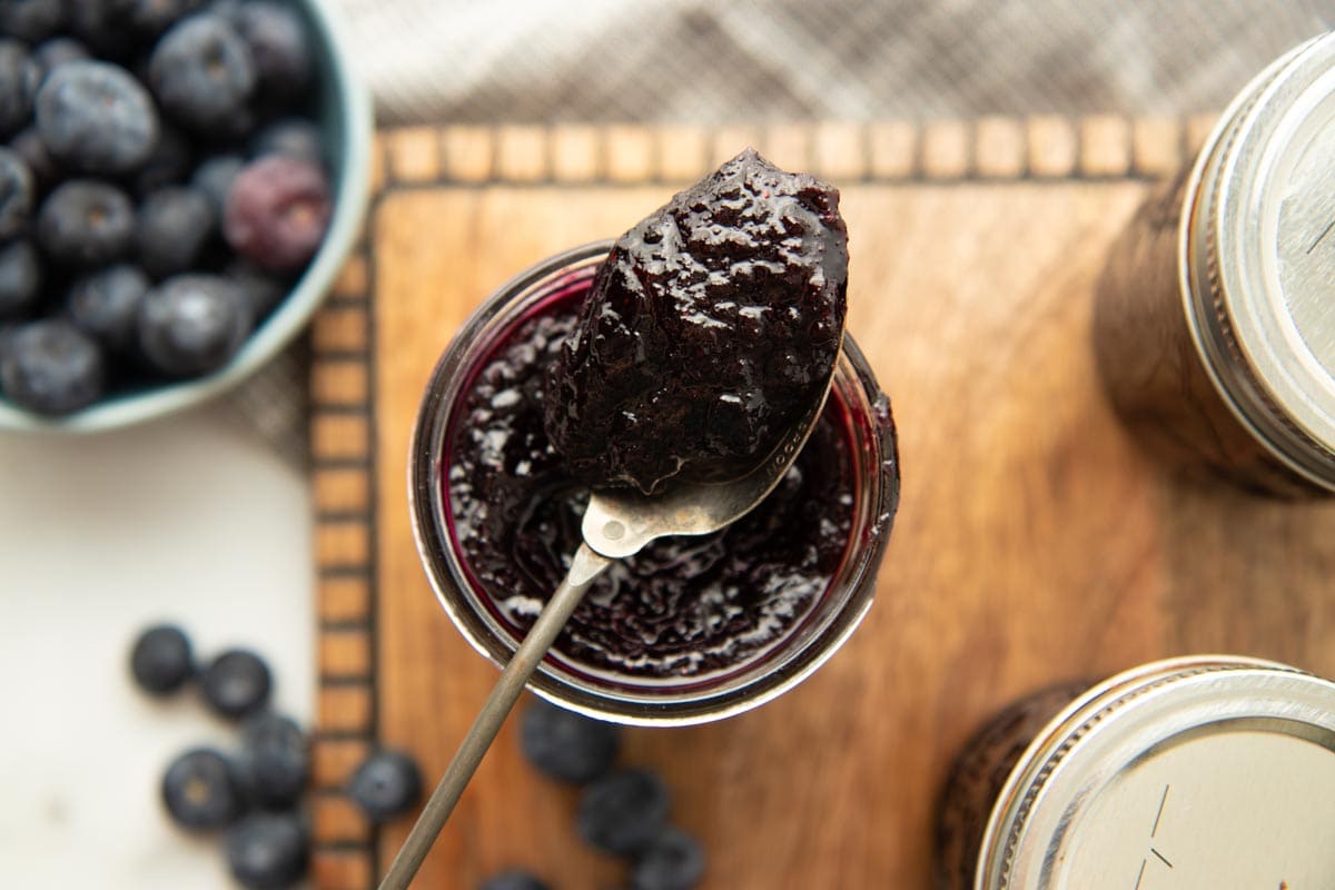 Overhead of a dollop of berry jam on a spoon resting atop an open jar of jam.