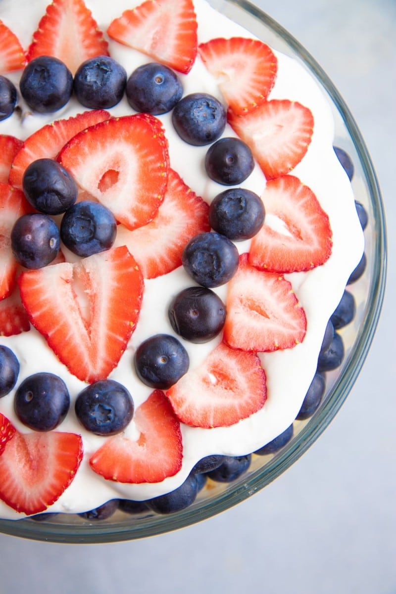 Top view of a festive berry trifle showing a red, white, and blue design using fresh strawberry slices and blueberries arranged in rings over the white cream topping.