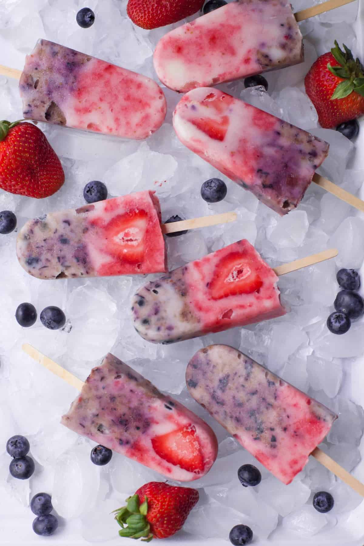 Six berry popsicles lay on a bed of ice