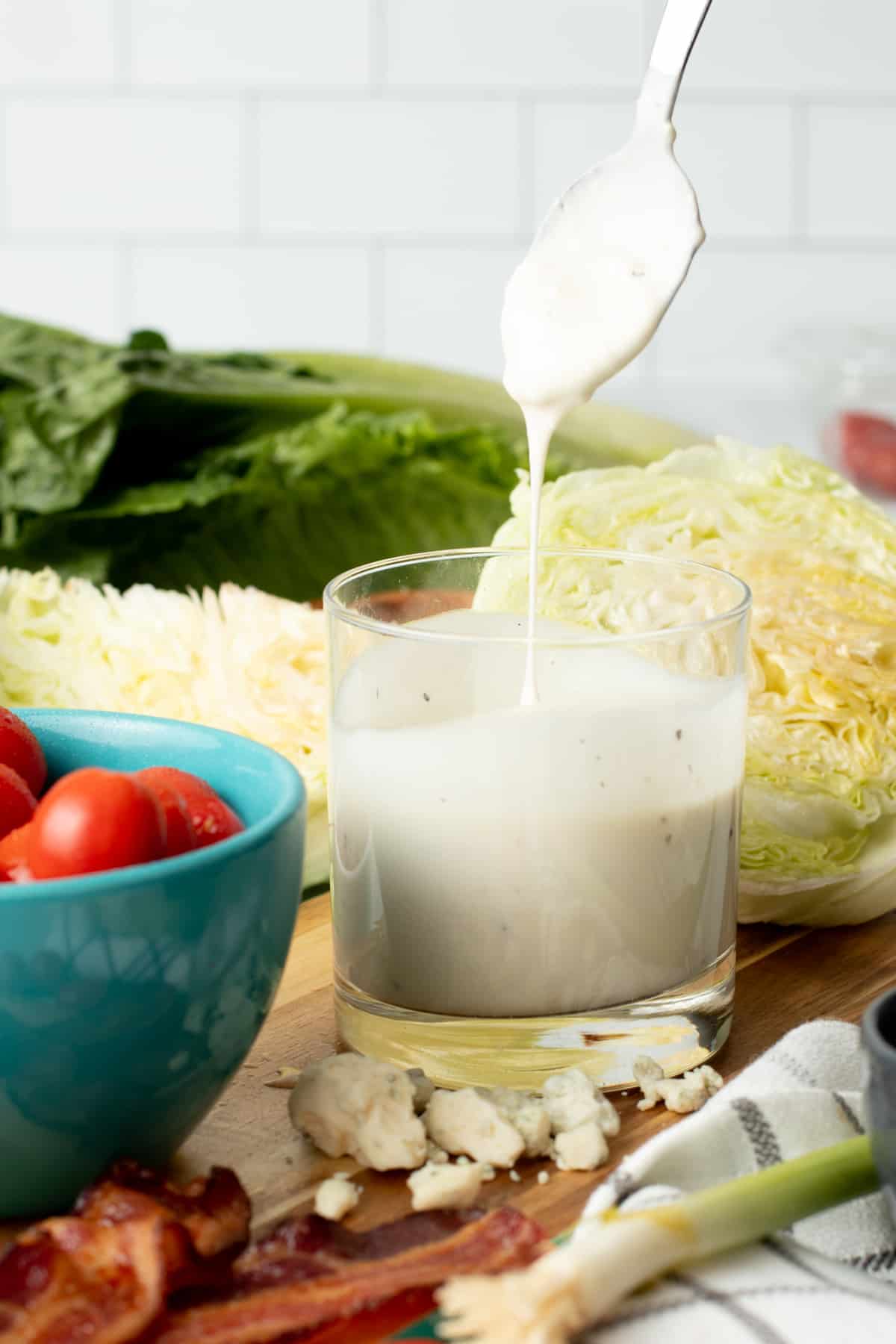 A spoon drizzles blue cheese dressing into a glass of dressing.