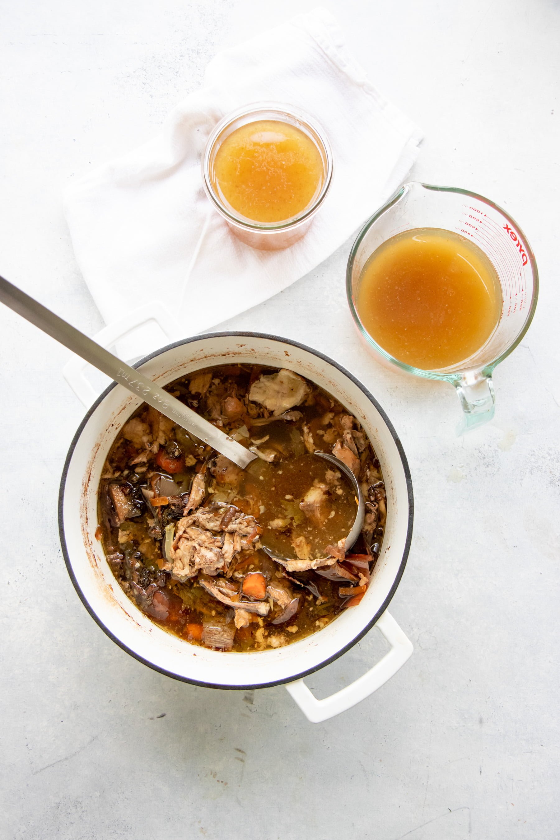 Overhead shot of finished bone broth in a large stockpot, with a glass Pyrex measuring cup and glass jar of bone broth