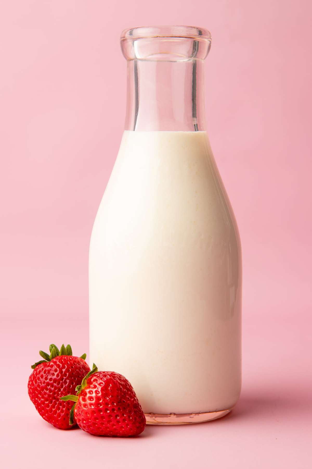 Close-up of glass carafe filled with finished kefir and two ripe, red strawberries beside it.