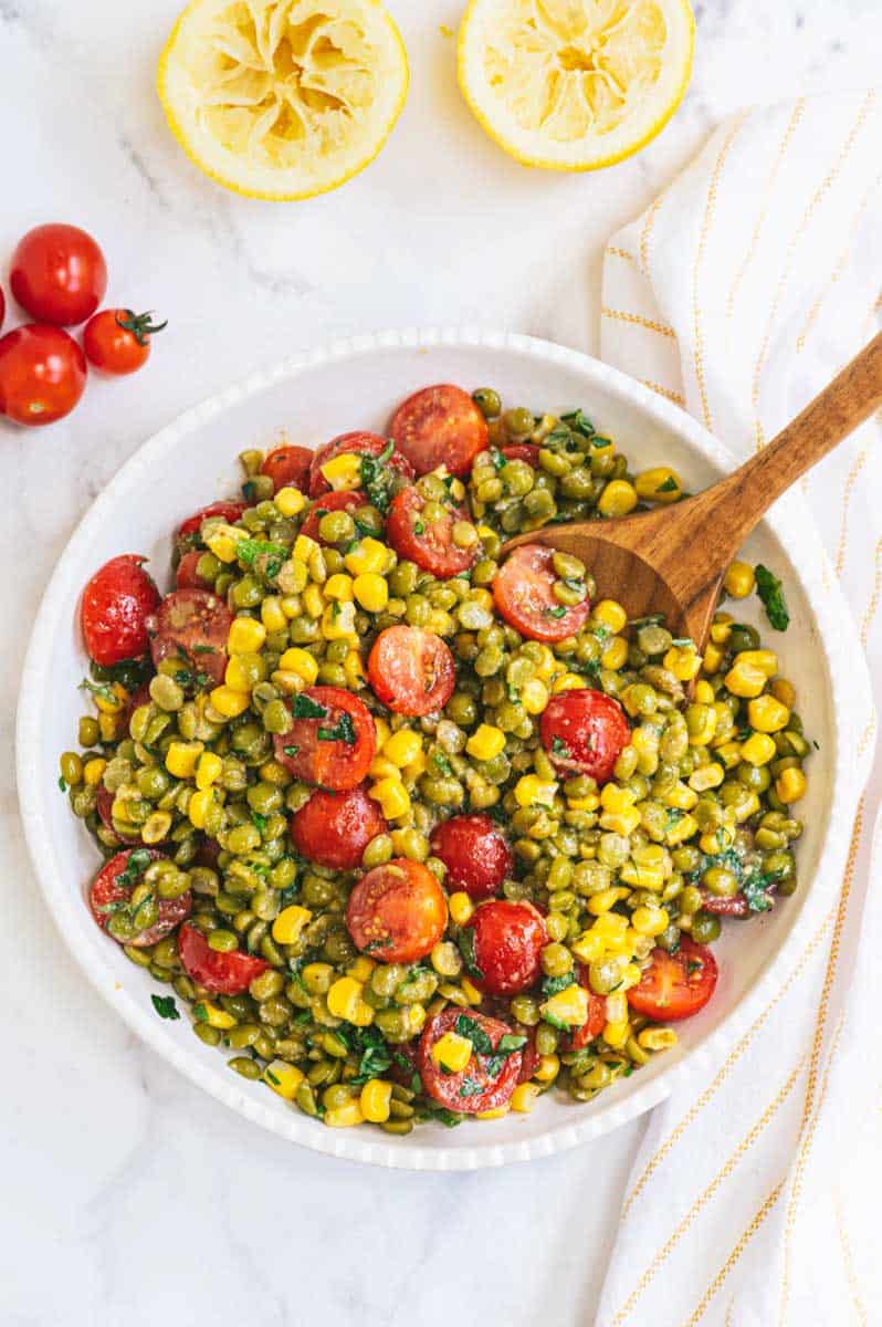 Overhead of serving bowl full of finished split pea salad with wooden serving spoon scooping up the first serving.