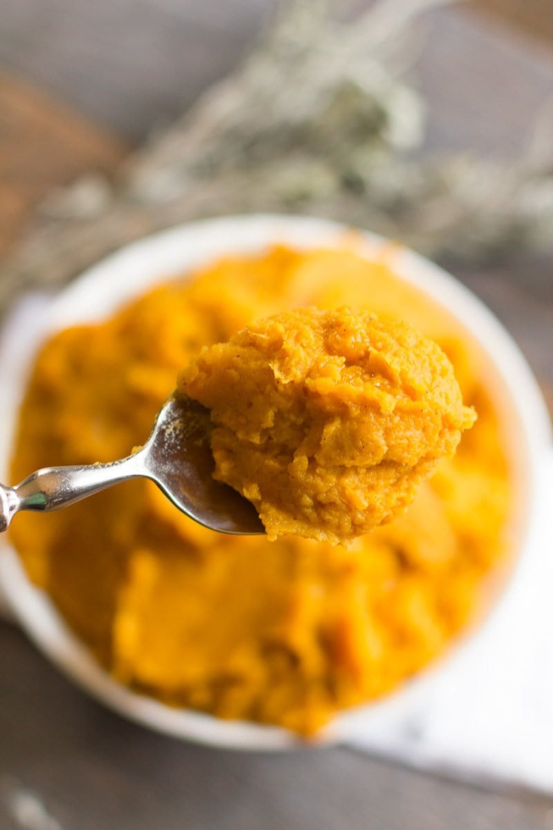 A spoon holds a bite of mashed sweet potatoes over a bowl.