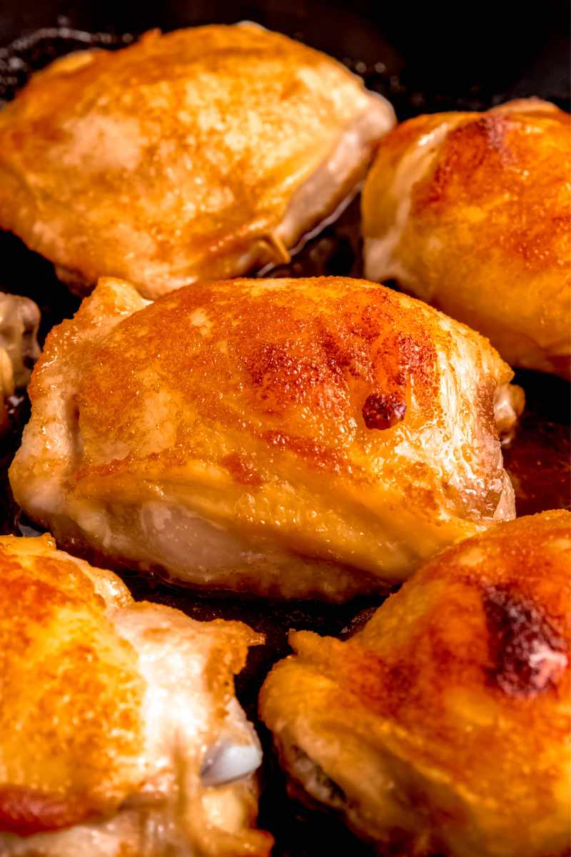 Tight view of a brown sugar chicken thigh in the center of a skillet with other thighs around it, all perfectly cooked and ready to serve.