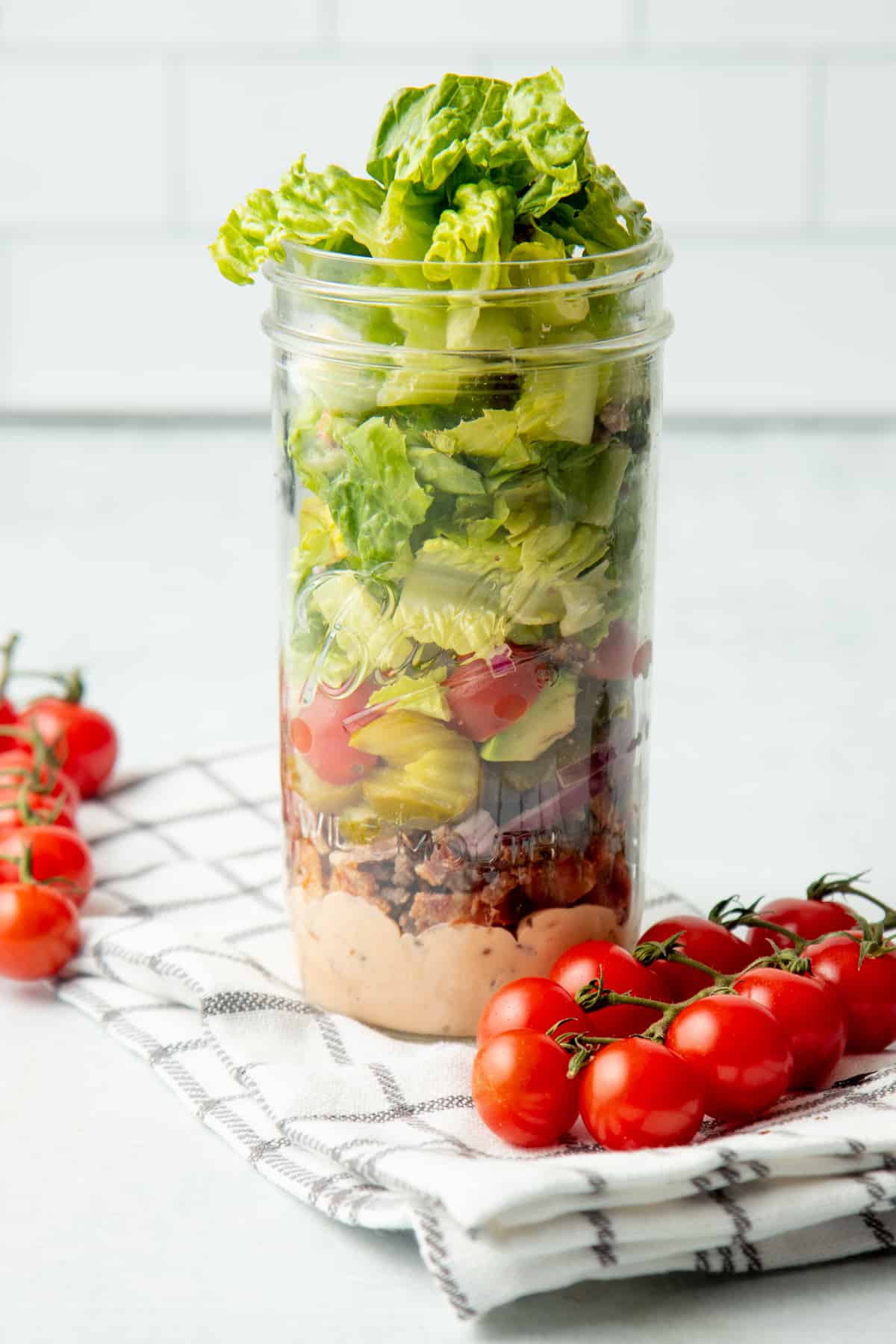 Ingredients for a burger bowl salad are layered in a wide-mouth mason jar