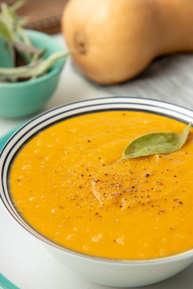 Close view of a full bowl of butternut squash soup topped with a sage leaf and cracked pepper.