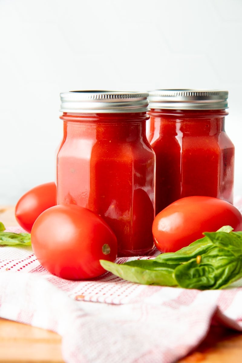 Two finished jars of basic sauce with fresh roma tomatoes and basil.