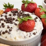 A bright red strawberry rests in a bowl of creamy dessert dip with more fresh berries and waffle cones around it. A text overlay reads, "Super Easy Cannoli Dip."