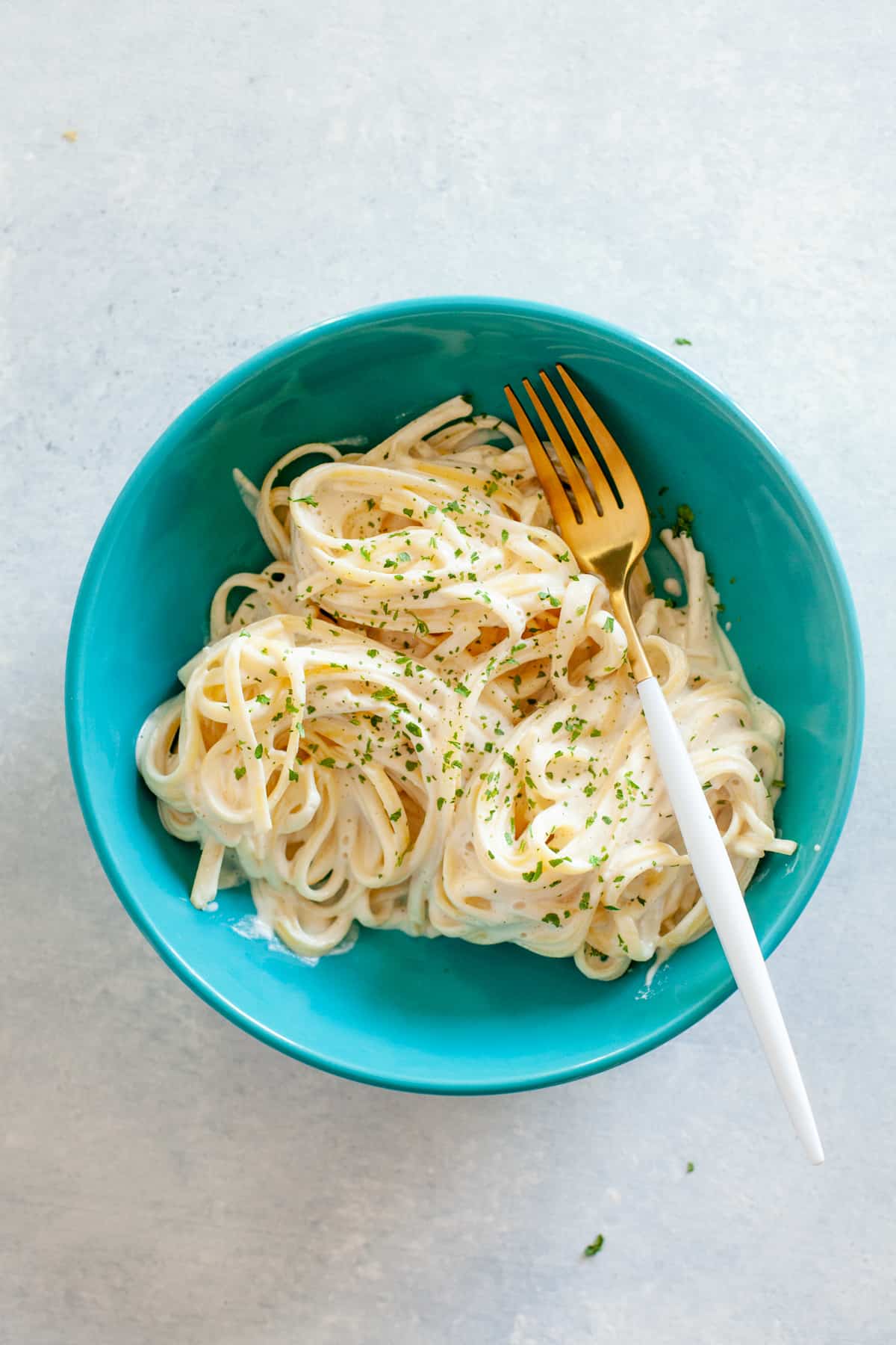 Turquoise bowl of fettucine noodles in a vegan cashew alfredo sauce.