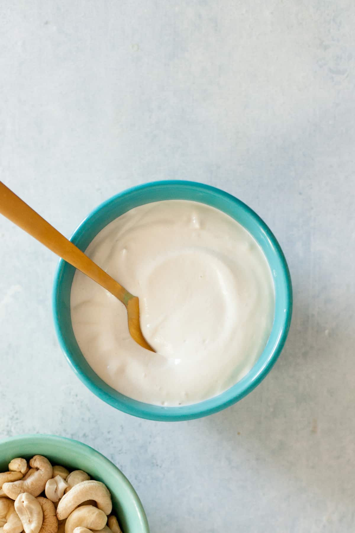 Small turquoise bowl filled with cashew cream. A gold spoon dips into the bowl.