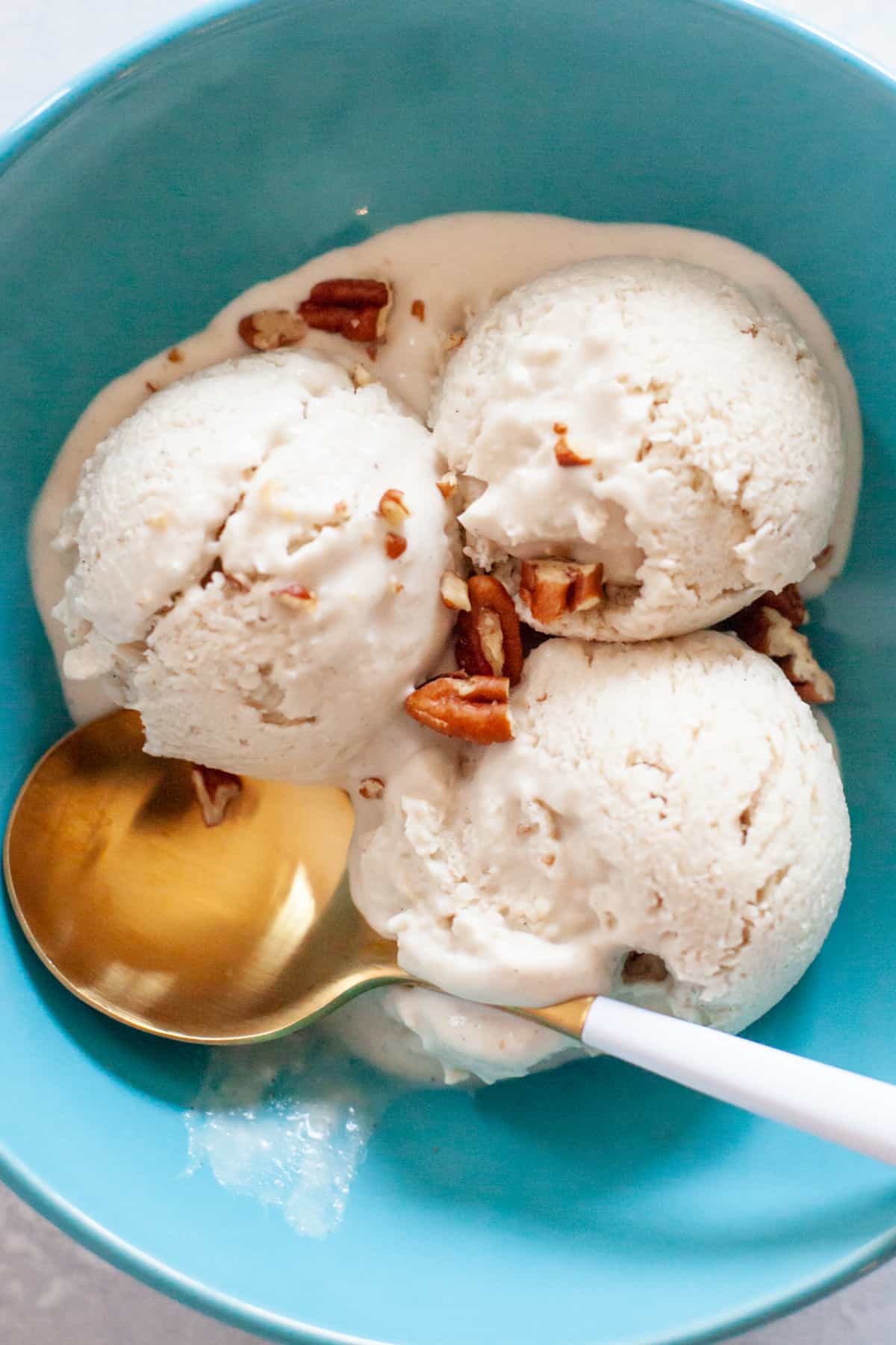 A gold spoon sits in a turquoise bowl with 3 scoops of vegan ice cream.