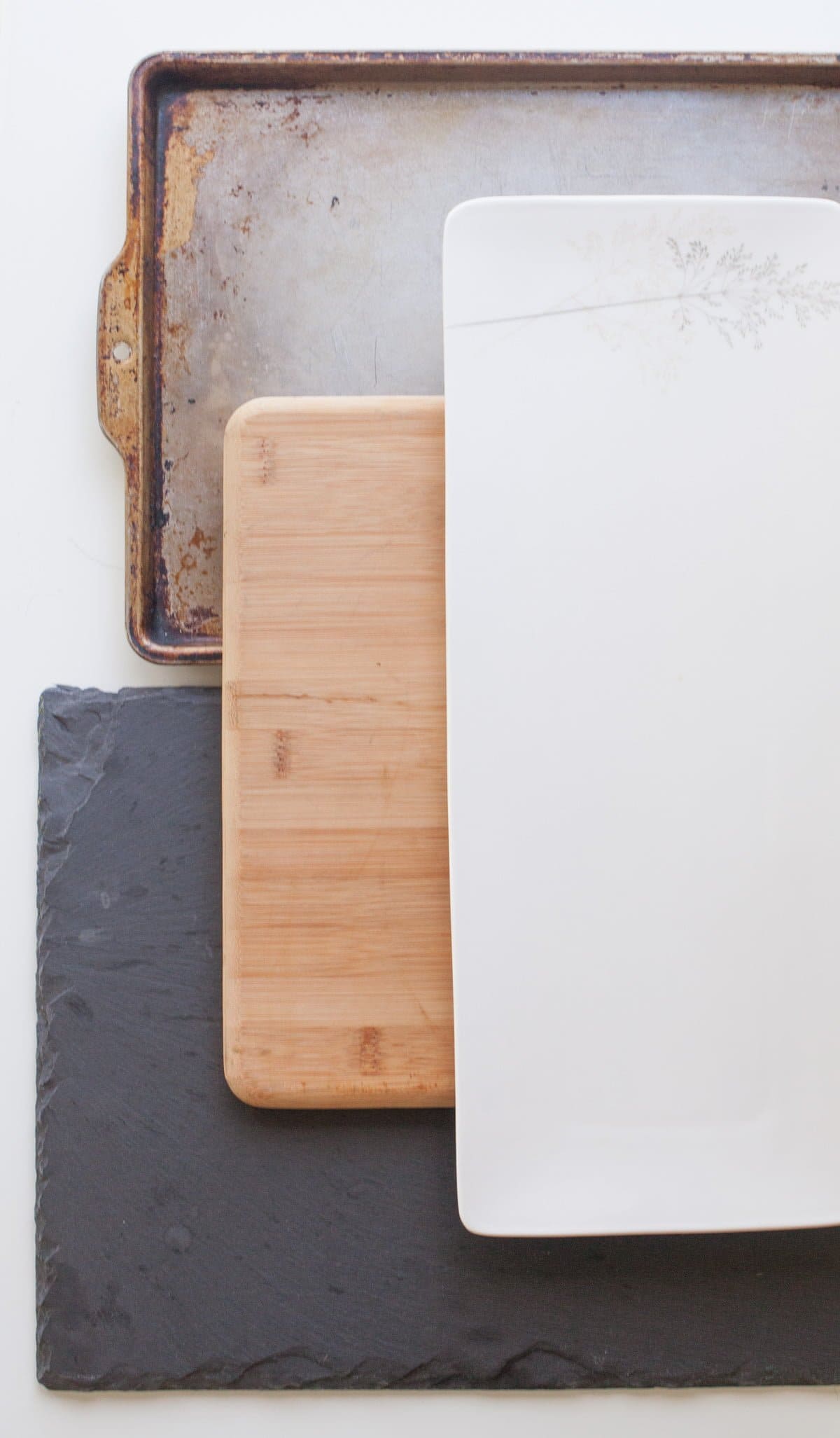 Stack of boards to use for a cheese board - slate platter, bamboo cutting board, a baking sheet, and a white board.