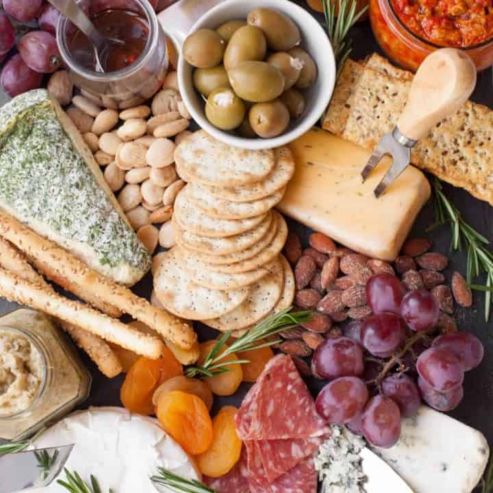 Close up of a cheese board with cheeses, crackers, olives, fruits, and almonds.