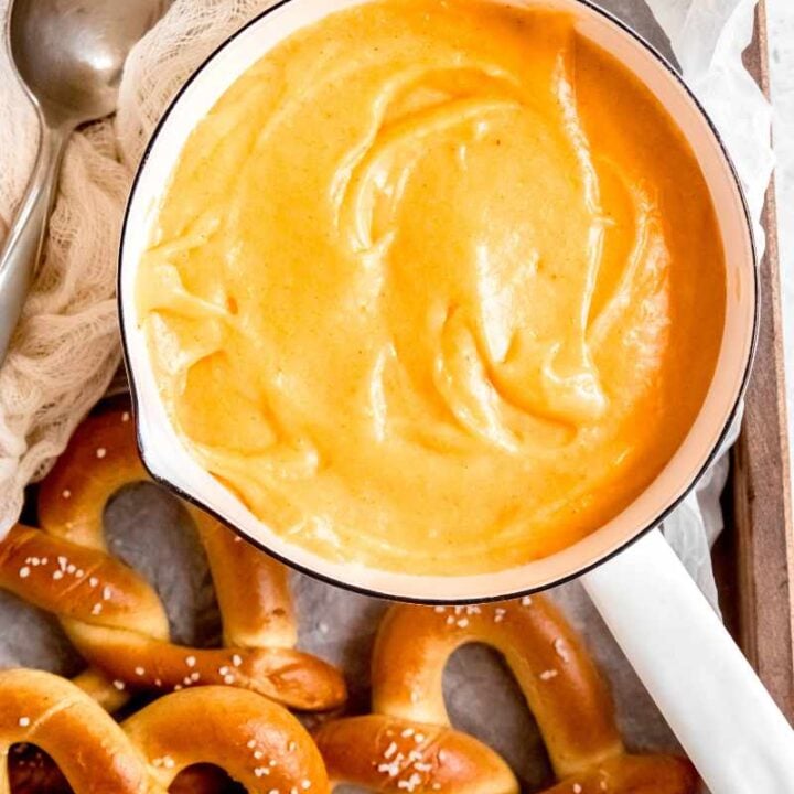 Overhead of a white saucepan filled with a warm cheese dip appetizer with soft pretzels around it.