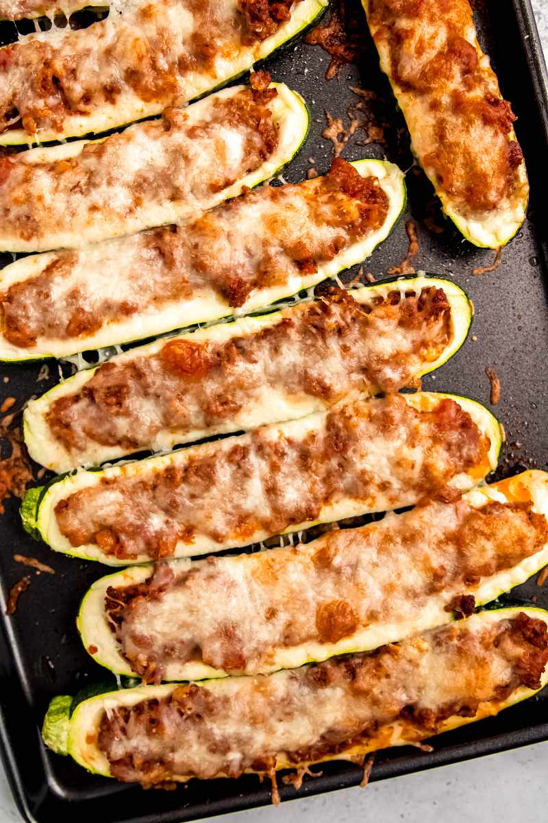 Top view of cheesy baked zucchini boats on a dark baking sheet.