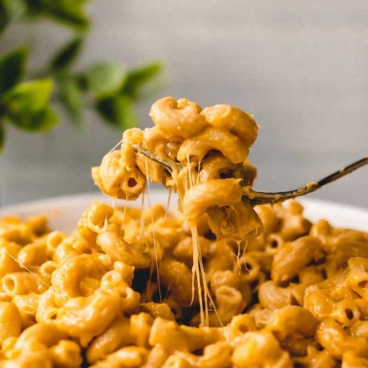 Close view of cheesy strands as a fork scoops up a bite of instant pot mac and cheese from a white bowl.