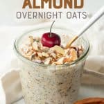 A spoon rests in a glass jar of cherry and almond overnight oats. The oats are garnished with a whole fresh cherry. A text overlay reads "Cherry Almond Overnight Oats."