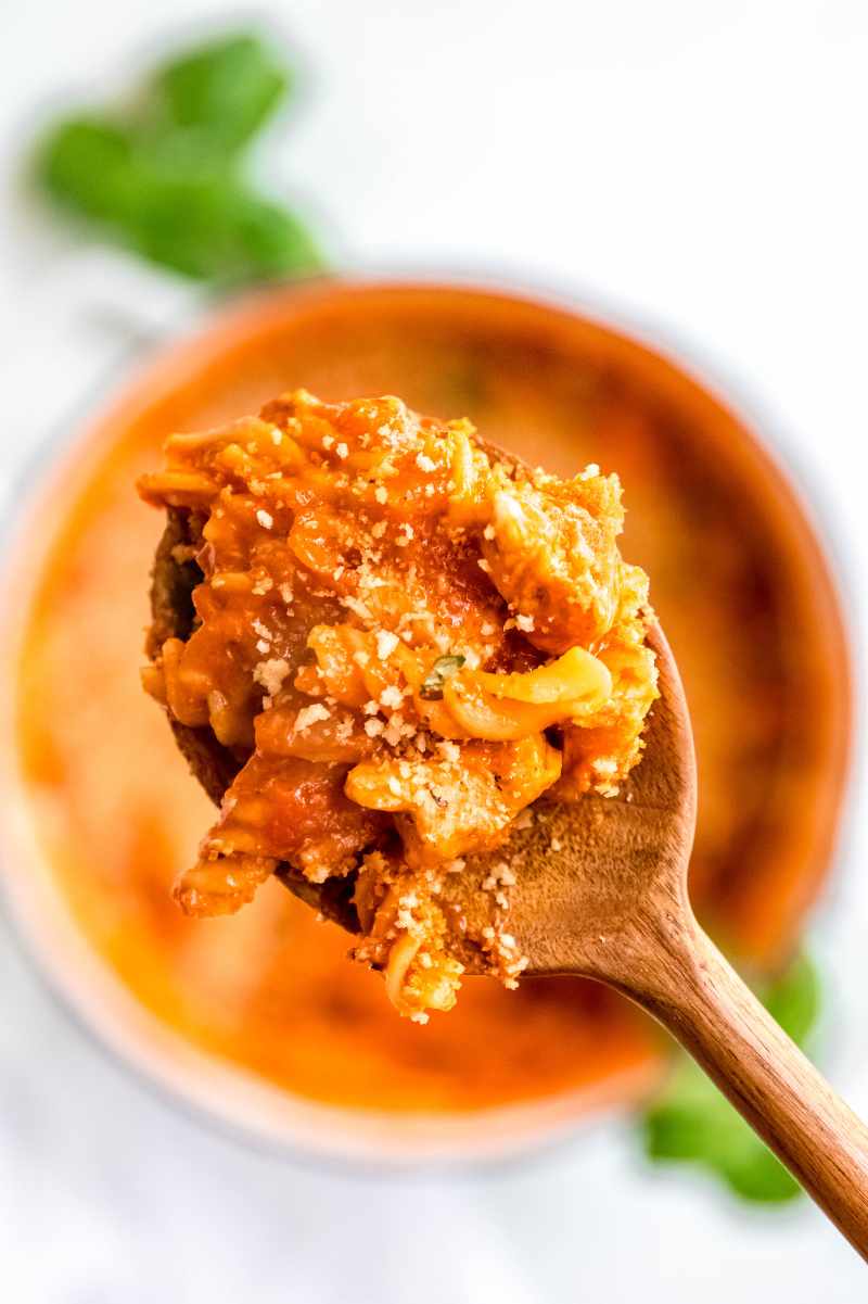 Close view of a scoop of one-pot chicken parmesan pasta on a wooden spoon.