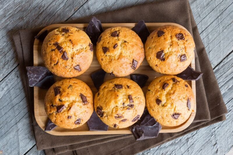 Top view of six chocolate chip muffins on a bamboo serving plate with extra chocolate around.