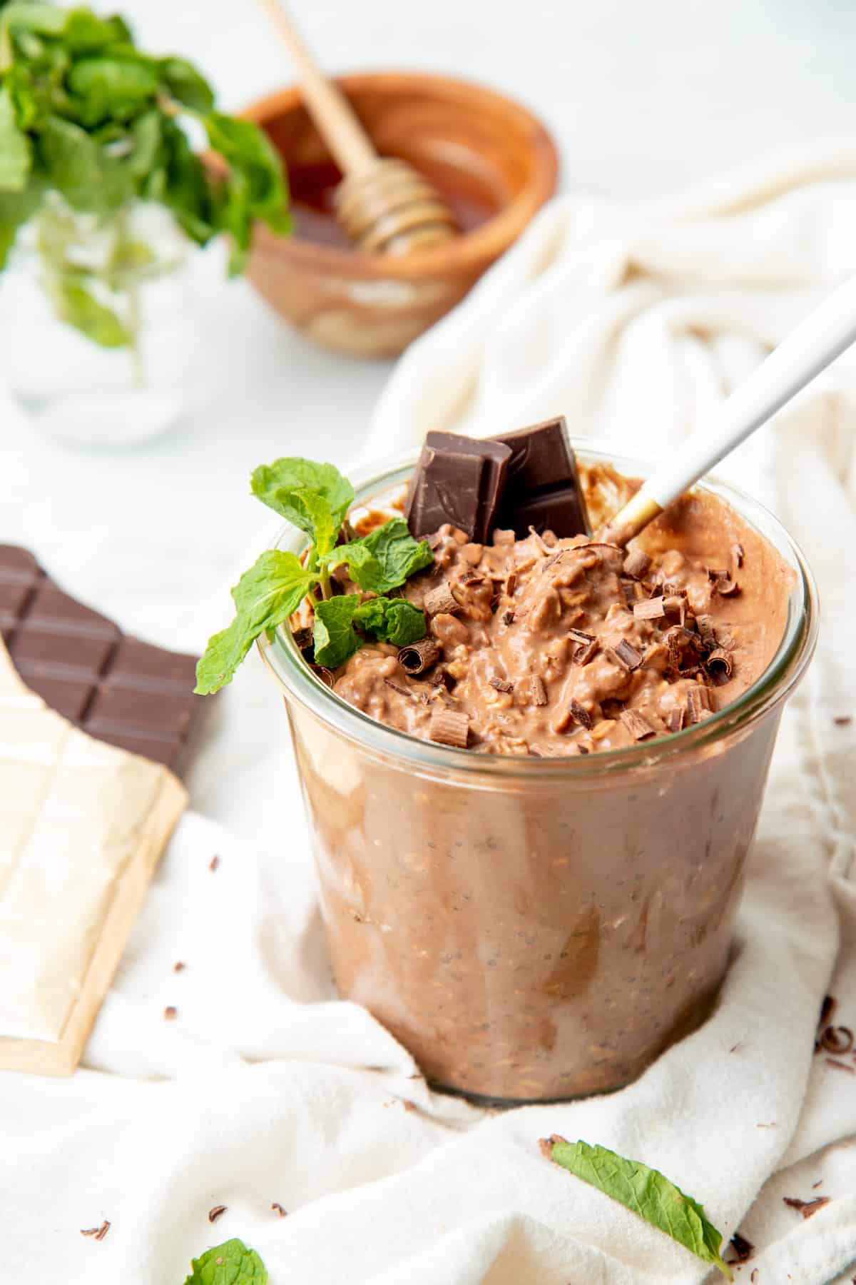 Overnight oats fill a glass jar. A small bowl of honey and an opened chocolate bar surround the jar.