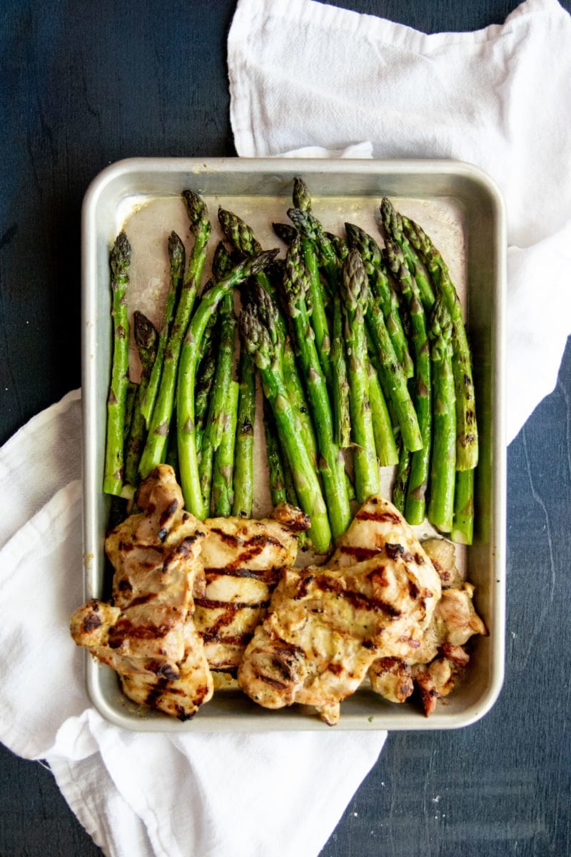 Overhead shot of grilled chicken and asparagus on a baking sheet