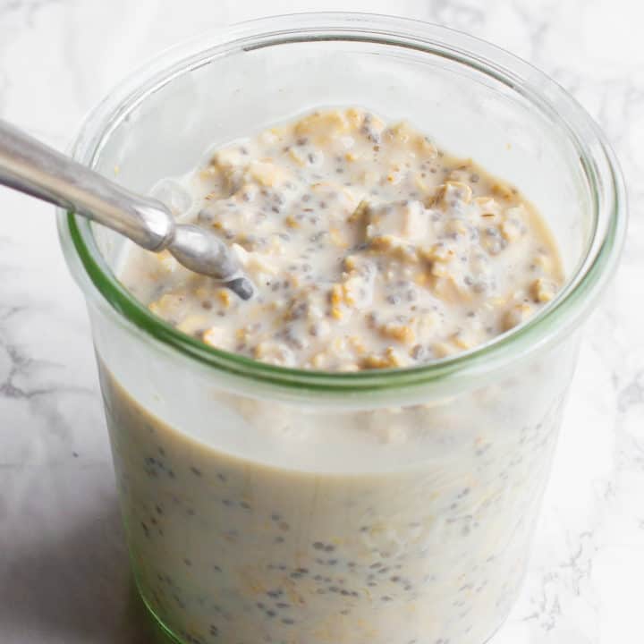 A clear glass jar filled with overnight oats, with a spoon sticking out.