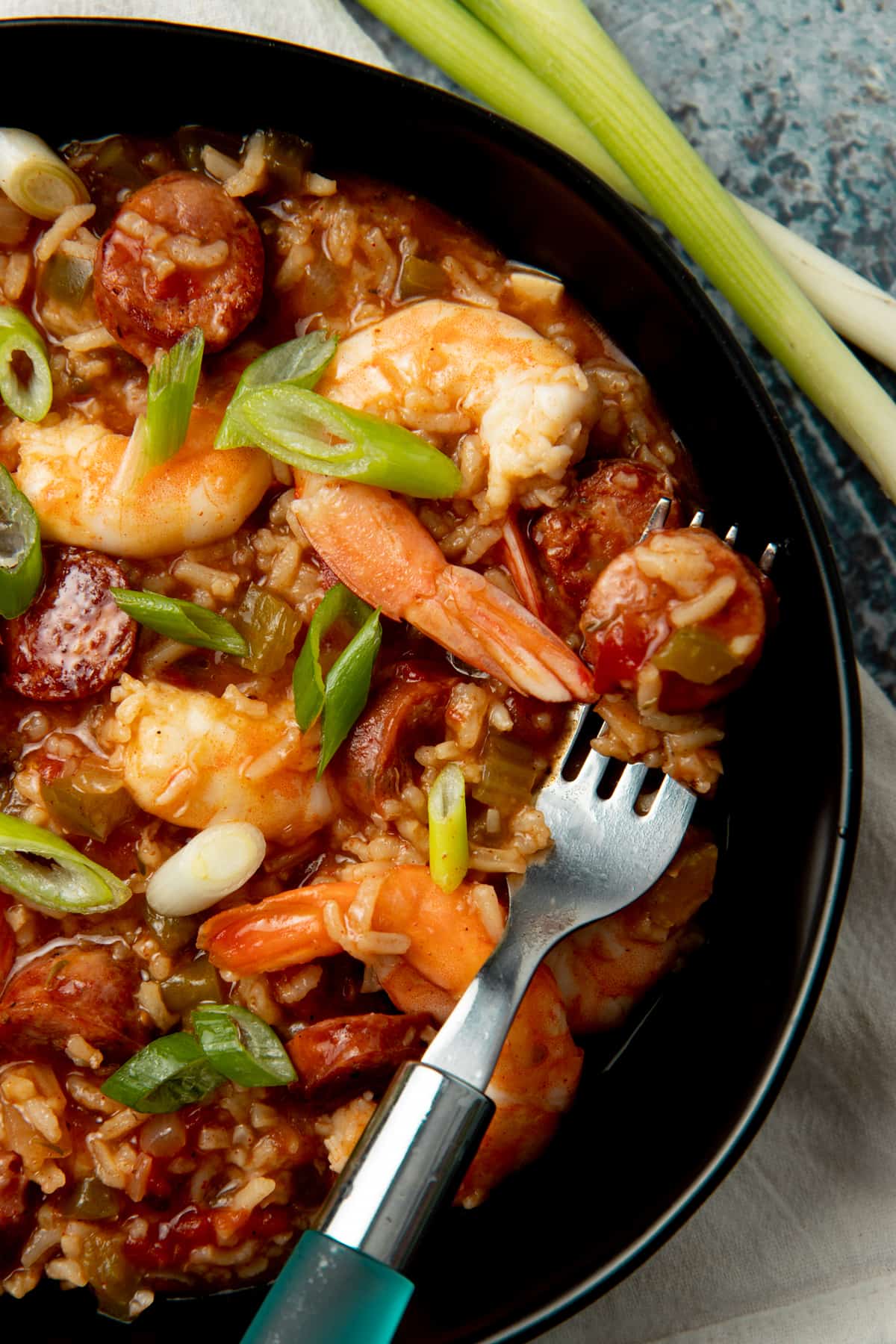 A piece of sausage rests on a fork inside a bowl of jambalaya.