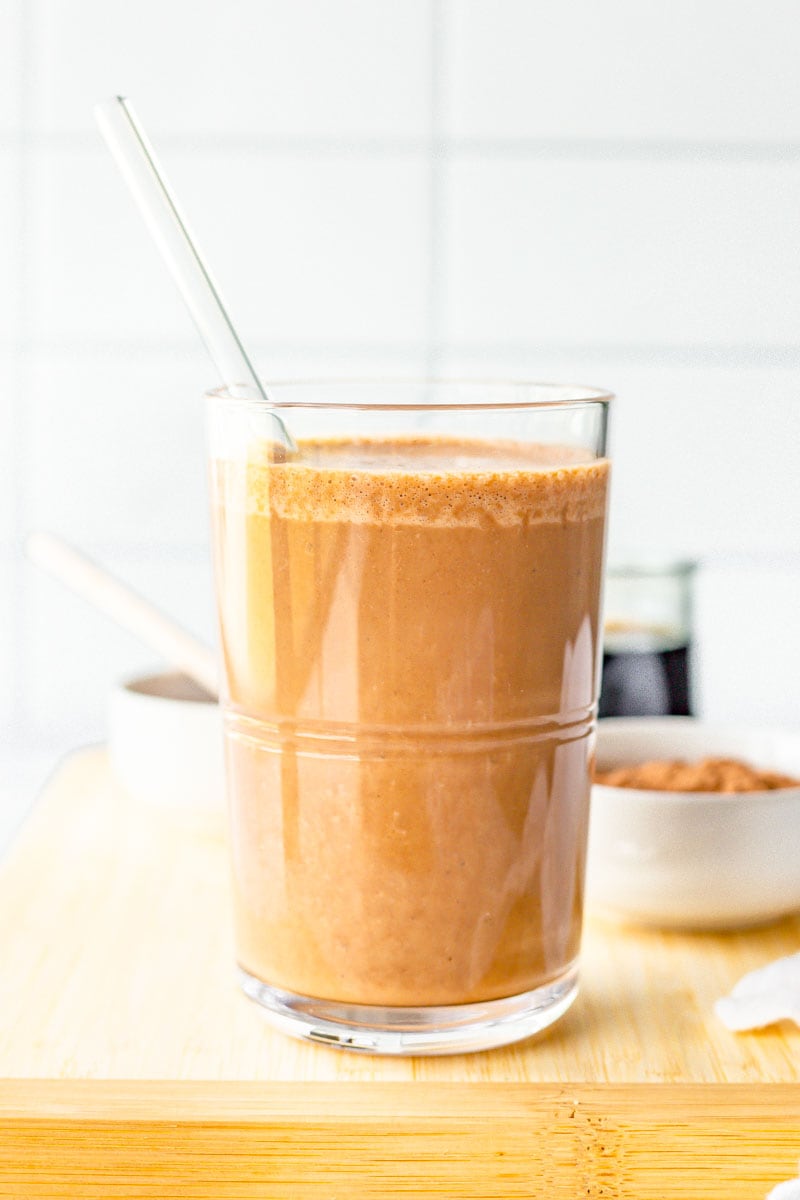 Close up of chocolate coffee smoothie in a glass with a glass straw on a cutting board.