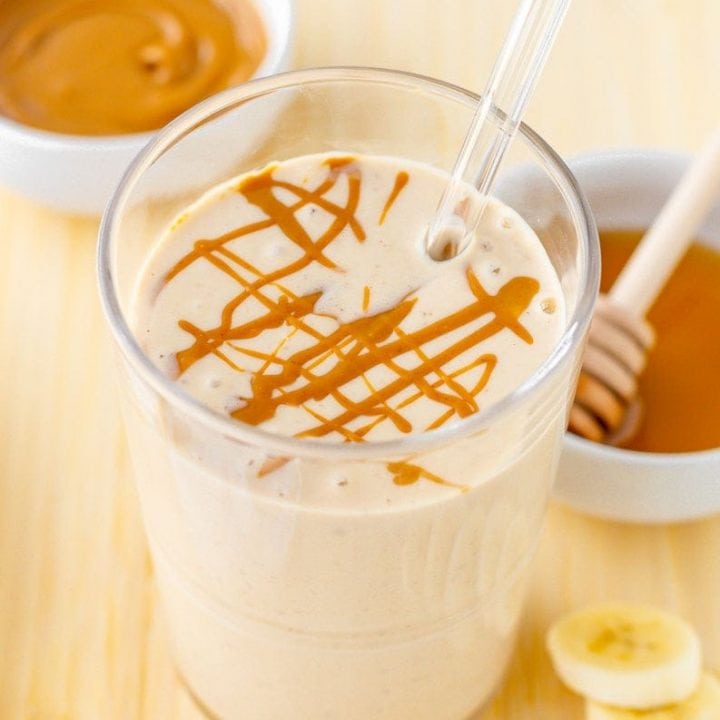 Close-up of finished smoothie with peanut butter drizzle and fresh ingredients around it.