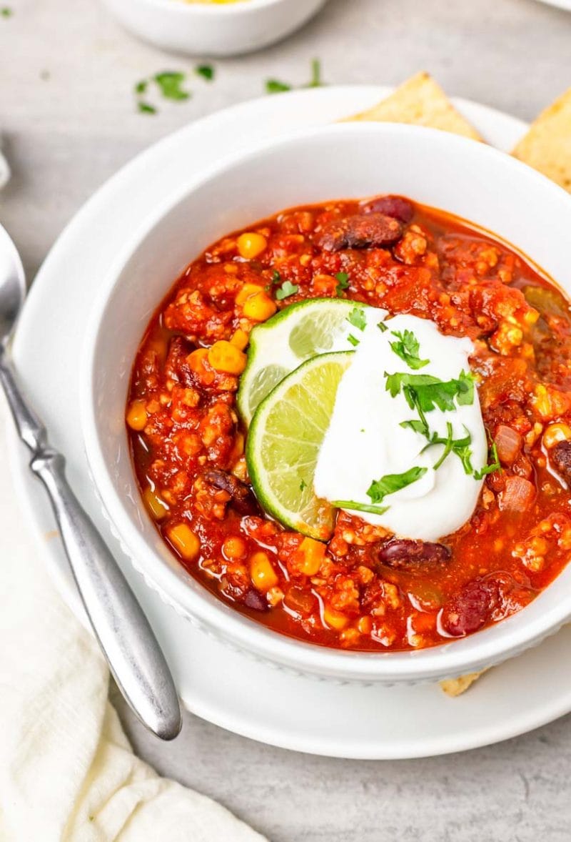 Close-up of full bowl of taco chili on a plate with spoon and tortilla chips.