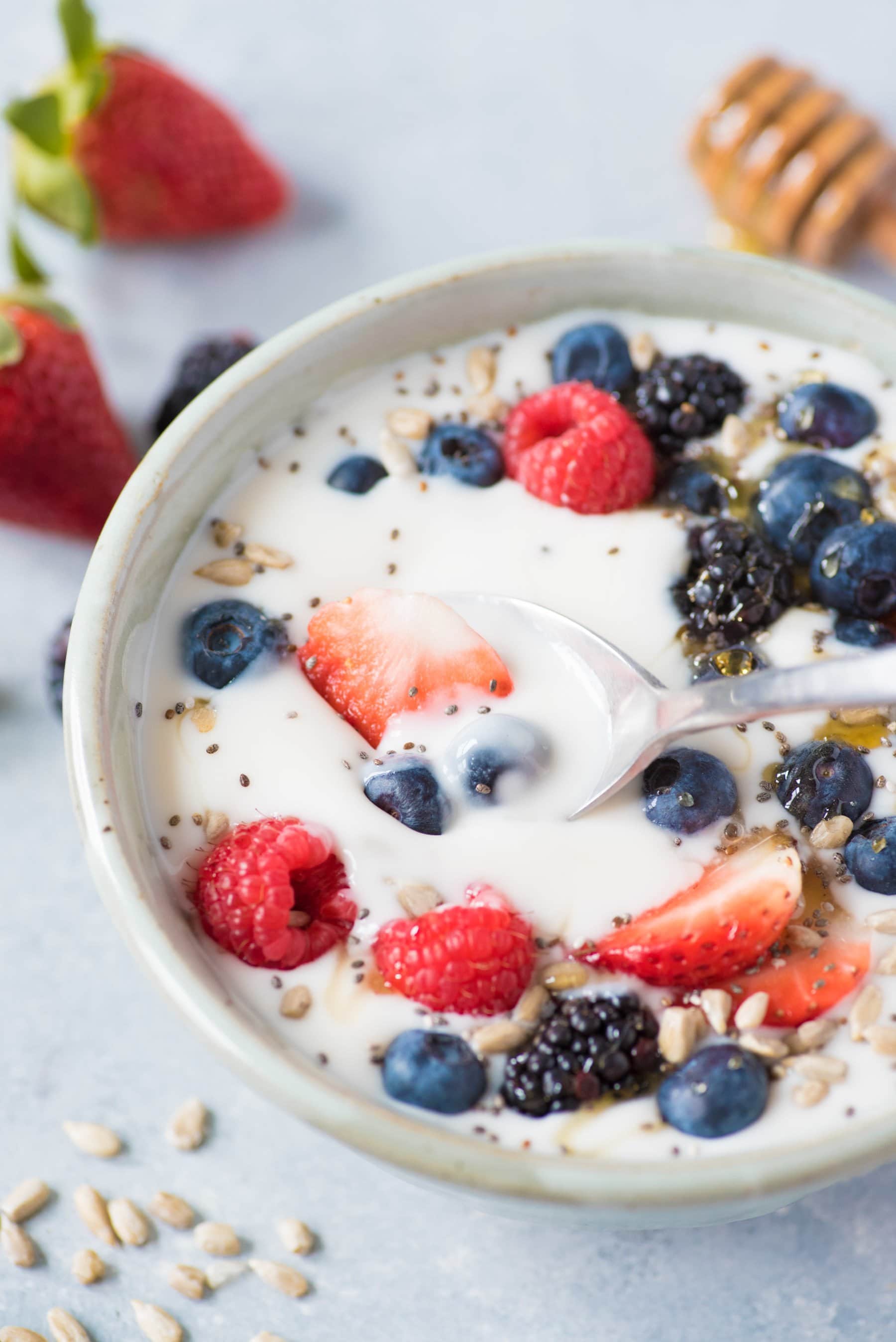 Side angle shot of a spoon and bowl of Instant Pot coconut yogurt topped with mixed berries, seeds, and honey